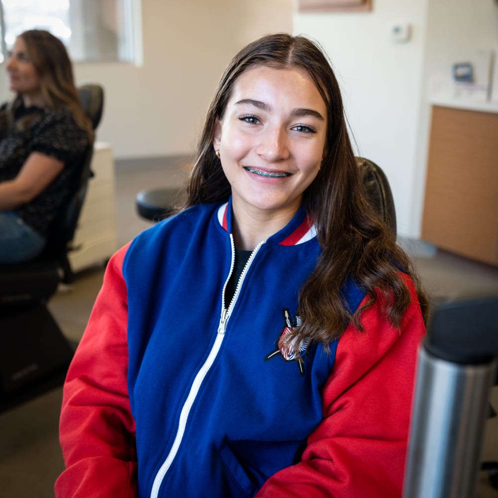 A teenage girl with a blue and red sweater smiles showing her braces.